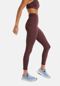 Leggings bordeaux avec taille haute, dotés de poches latérales et d'une texture lisse. Assortis à des chaussures de sport bleu clair.