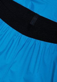 Blå tygshorts med en strukturerad yta, som har en bred svart elastisk midjeband och veckad detalj längs midjan.