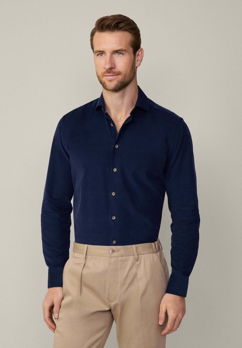 Camisa de manga larga de color azul marino, hecha de una tela con un acabado texturizado, que presenta un cuello abotonado y botones de un color contrastante.
