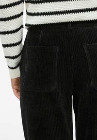 Melnu korduroja bikses ar plašiem legiem, vertikālu ribu struktūru un divām aizmugures kabatām. Komplektā ar svītrainu adītu džemperi.