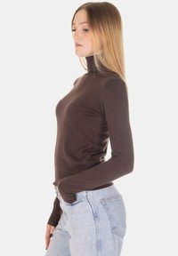 Maglione dolcevita marrone dal taglio aderente, con maniche lunghe e texture morbida, abbinato a jeans azzurri a vita alta.