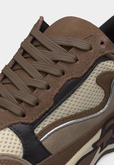 Κοντινό πλάνο καφέ αθλητικού παπουτσιού με υφασμάτινη υφή, πάνελ από σουέντ, καφέ κορδόνια και λεπτομέρειες σχεδίασης σε στρώσεις σε μαύρο και μπεζ.