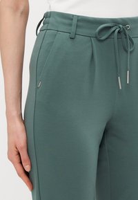 Groene joggingsbroek van zacht materiaal, met een elastische tailleband met trekkoord, zijzakken en een kleine logodetail.