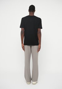 Μαύρη βαμβακερή μπλούζα κ�οντομάνικη με κλασικό λαιμόκοψη, συνδυασμένη με ανοιχτό γκρι παντελόνι με φαρδιά πόδια και ανοιχτόχρωμα αθλητικά παπούτσια.