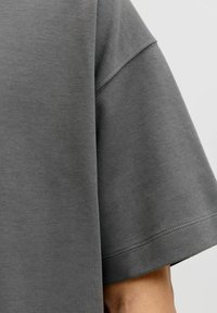 T-shirt en coton gris présentant une coupe décontractée, des épaules tombantes et des bords finis, offrant une texture douce et un design simple.