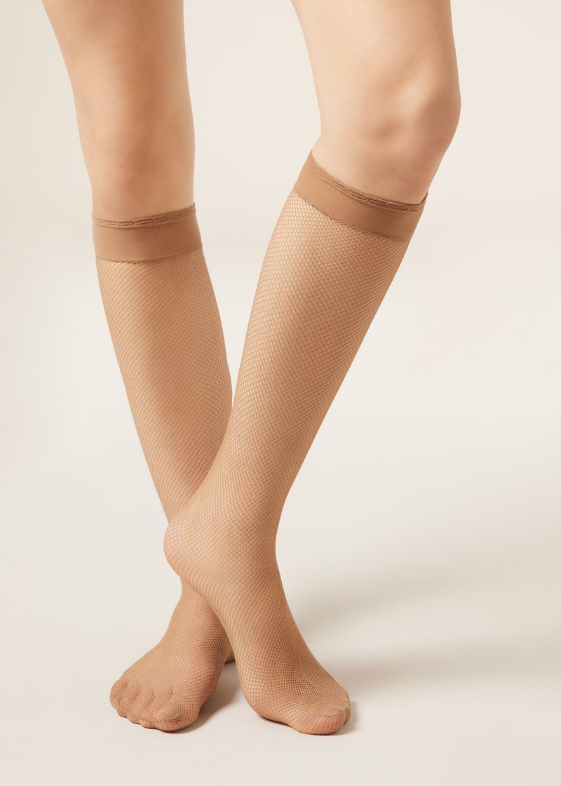 Beine, die durchsichtige beige knielange Netzstrümpfe mit verstärktem Bund am oberen Rand tragen, überkreuzt an den Knöcheln auf hellem Hintergrund.