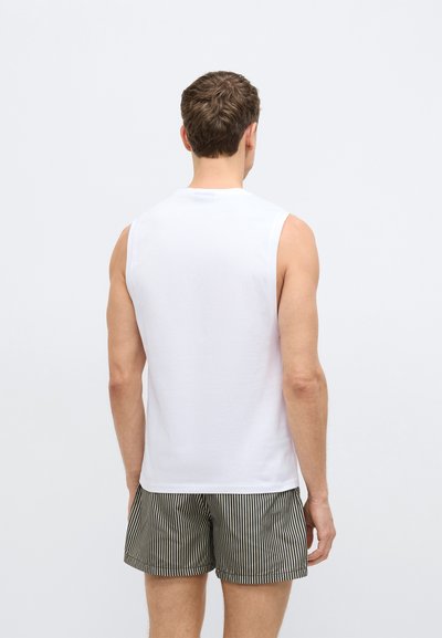 Biała bawełniana koszulka na ramiączkach z okrągłym dekoltem, zestawiona z szortami w szaro-białe paski. Brak widocznych logo ani wzorów.