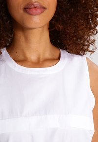 Top blanco sin mangas con un escote redondo, textura suave y un sutil detalle de costura horizontal. Enfóquese en la ligereza y el caído de la tela.