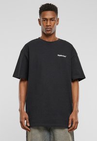 Sort bomuld t-shirt med korte ærmer, rund hals og hvid tekst, der står "glemte ansigtter" på venstre brystområde.