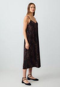 Schwarzes und burgunderfarbenes ärmelloses Midikleid mit floralem Muster; hat einen V-Ausschnitt und ein fließendes Design. Kombiniert mit schwarzen flachen Schuhen.