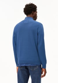 Maglione blu lavorato a maglia con colletto, polsini e orlo a costine, presenta un retro texturizzato e un aspetto a strati sopra una camicia blu.