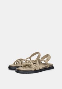 Sandale bej din suede cu curele din sfoară răsucită, talpă plată neagră, design cu vârful deschis și suport pentru gleznă. Tălpică texturată pentru confort.