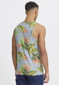Ermeløs tanktop i lyseblå med livlige grønne og oransje tropiske blad- og blomstermønstre. Mykt stoff og løs passform.
