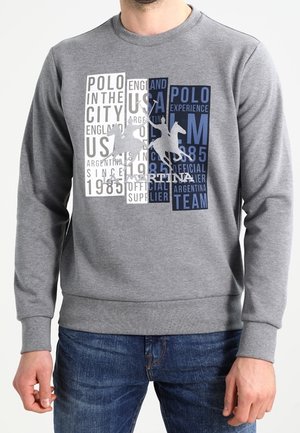 Sweatshirt gris en mélange de coton. Présente un texte graphique en blanc et bleu, représentant "Polo" avec un motif de cheval et l'année "1985."