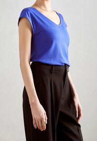 Blue cotton short-sleeve V-neck top, paired with black high-waisted wide-leg trousers, featuring a textured fabric and subtle pleats.