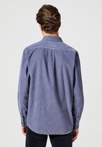 Camisa de pana azul con mangas largas, dobladillo recto y puños abotonados. Presenta un pliegue en la parte posterior y un diseño de cuello clásico.