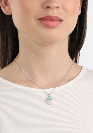 Damen-Ausschnitt mit silberner Kettenhalskette, die einen Schmetterling und einen abstrakten Blumenanhänger zeigt, trägt ein geripptes weißes Oberteil.