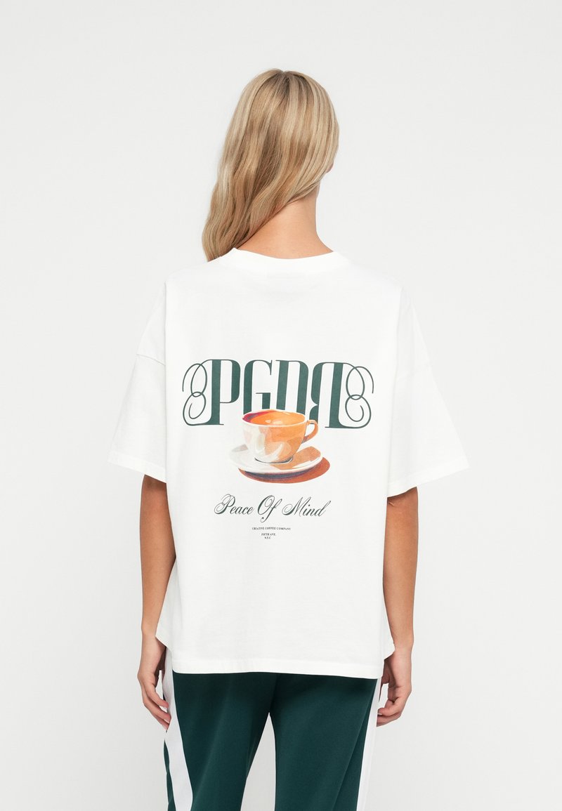 Tricou alb din bumbac, cu un grafic colorat al unei cești și farfurii, având textul "PGDR" și "Pacea Minții". Design lejer.