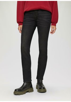 Jean en denim noir avec une coupe slim, présentant une texture subtile. Associés à des bottines noires avec une semelle chunky verte.