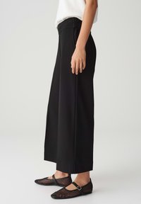 Black wide-leg pants with an elastic waistband, paired with black mesh flats featuring a strap. Smooth texture, minimalist design.