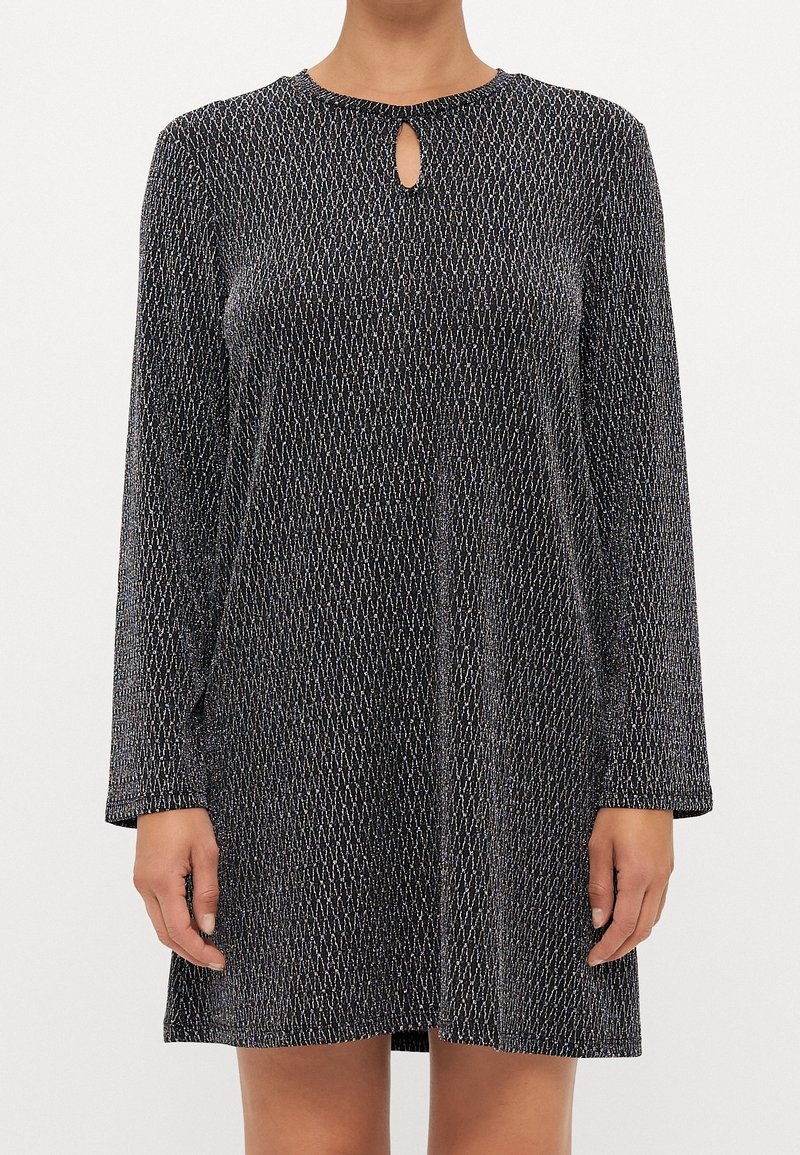 Femme portant une robe à manches longues noire et argentée avec une petite découpe en forme de goutte près de l'encolure.