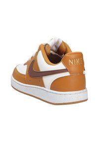 Sneaker Nike avec une tige en cuir marron et blanc, un col rembourré et une semelle texturée. Présente un swoosh marron et une semelle intermédiaire blanche.