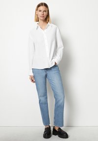 Weißes Hemd mit Kragen, kombiniert mit hellblauen geraden Jeans und schwarzen Plateau-Loafern. Weicher Stoff, lockere Passform.