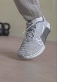 Light gray athletic shoe with a breathable mesh upper, classic lacing, and textured sole. Features swoosh logo and accent design on the heel.