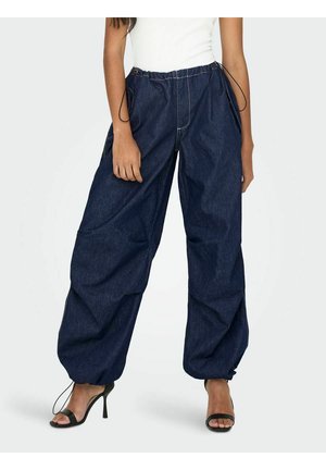 Donkerblauwe denimbroek met een losse pasvorm, een tailleband met trekkoord en opgerolde boorden. Gecombineerd met zwarte hoge hakken.