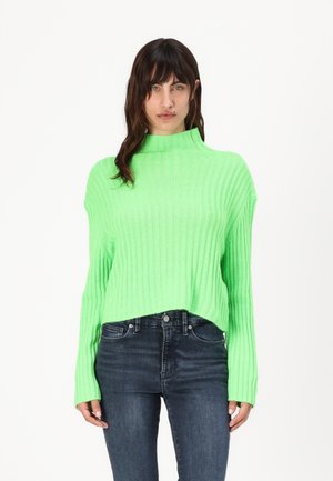 Ribbed, bright green sweater with a high neckline and fitted cuffs, paired with dark blue jeans. Sweater has a loose, cropped fit.