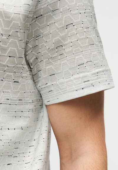Κοντομάνικο t-shirt σε ανοιχτό γκρι με υφασμένο ζιγκ-ζαγκ μοτίβο σε πιο σκούρο γκρι και μαύρες λεπτομέρειες στο ύφασμα.