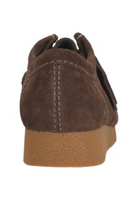 Ruskea mokkasukkanen, jossa on teksturoitu kumipohja. Ominaisuuksiin kuuluu pyöreä takaosa, jossa on näkyvät saumat ja nahka-aksonit kantapään läheisyydessä.