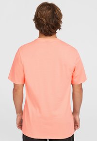 Camiseta de manga corta en coral fluorescente, hecha de algodón suave. Cuenta con un escote redondo y un corte holgado con un dobladillo recto.