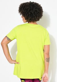 T-shirt à manches courtes vert fluo avec encolure ronde, texture lisse et coupe décontractée, associé à un legging à motifs.