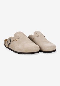 Zuecos de ante color beige con parte trasera abierta, punteras redondeadas, una correa ajustable y una suela de goma oscura texturizada. Presentan elementos de diseño minimalistas.