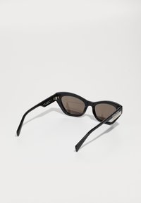 Ochelari de soare negri cu formă cat-eye, cu lentile închise, ramă din plastic neted și detalii metalice pe brațe cu accente de logo.