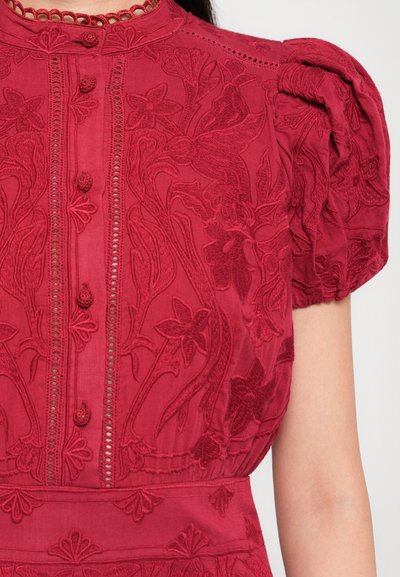 Rode geborduurde blouse met bloemenpatronen, met stof beklede knopen aan de voorkant, en pofkorte mouwen op de bovenste torso van een persoon.