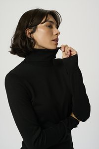 Pull à col roulé noir avec des manches longues, confectionné dans un tissu côtelé doux. Le col est haut et la coupe est ajustée au corps.
