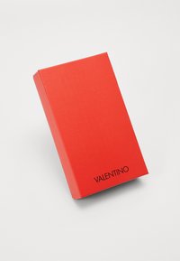 Piros téglalap alakú doboz, sima felülettel és matt finishel, a jobb alsó sarokban fekete "VALENTINO" felirattal.