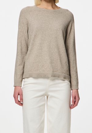 Pull léger marron fabriqué en matériau doux, avec un col rond, des manches longues et une coupe décontractée, associé à un pantalon blanc.