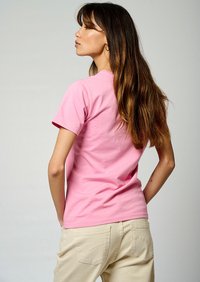 T-shirt en coton rose à manches courtes, col rond classique et coupe décontractée. Associé à un pantalon beige clair avec des poches arrière.