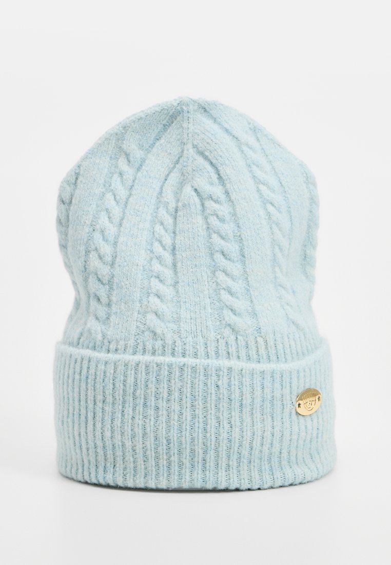 Hellblau gestrickte Mütze mit geripptem Bündchen, die ein strukturiertes Zopfmuster und ein goldfarbenes Metall-Logoetikett an der Seite aufweist.