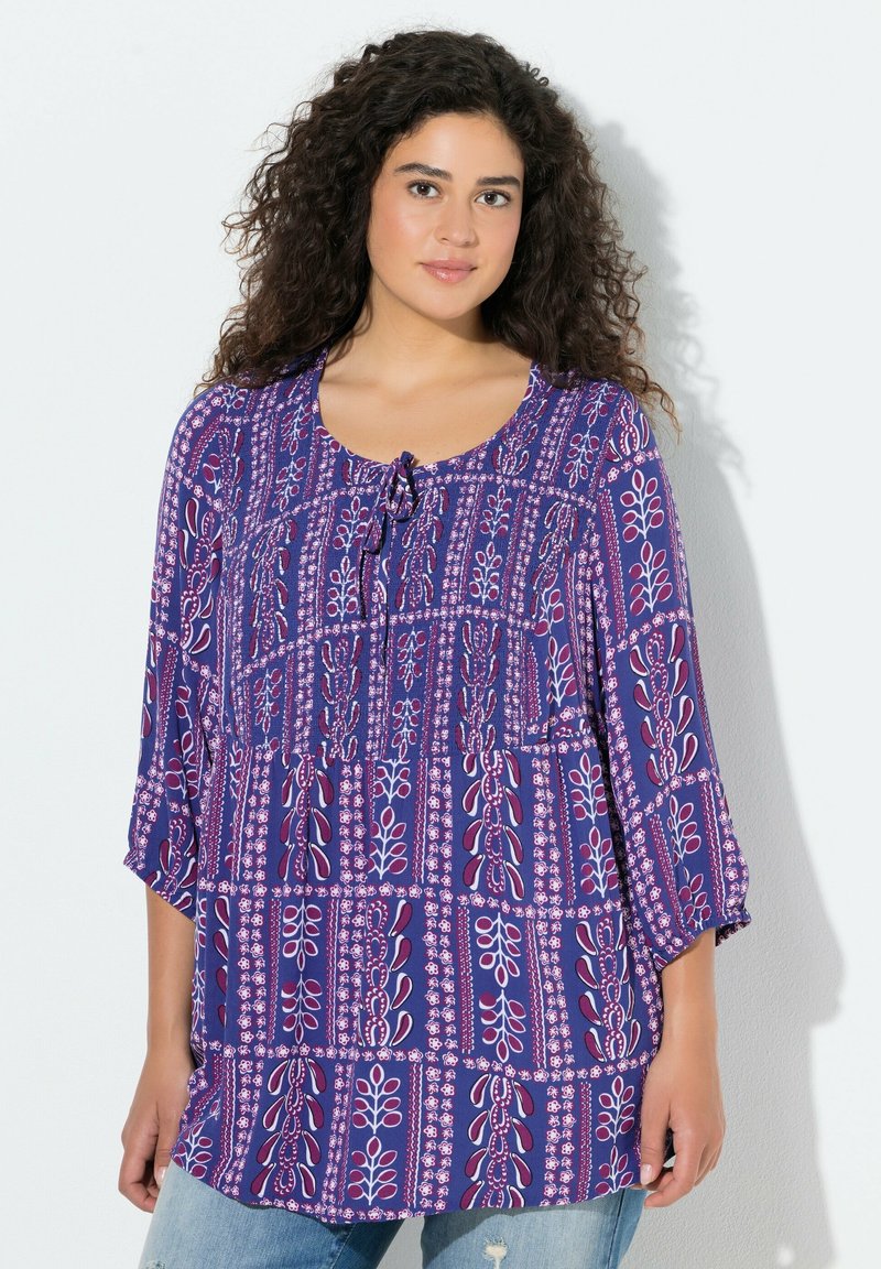 Fioletowo-różowa bluzka w wzory z rękawami do łokcia, okrągłym dekoltem i wiązaniem z przodu, wykonana z lekkiego materiału.