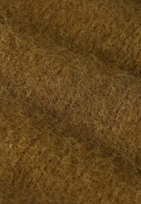 Tissu brun texturé mettant en avant des fibres douces et duveteuses. Le matériau semble dense avec des brins visibles, créant un aspect chaleureux et accueillant.