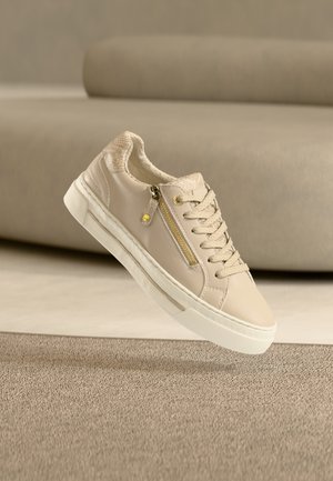 Baskets beige avec un accent texturé couleur tan et une fermeture éclair latérale. Caractérisées par des lacets ronds, une semelle en caoutchouc blanche et un design minimaliste.