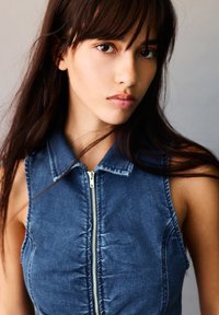 Denim sleeveless dress with a collared neck, front zipper, and stitched detailing, in a medium blue color with smooth texture.