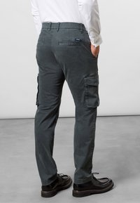 Tmavě šedé cargo kalhoty s uvolněným střihem, elastickým pasem, několika postranními kapsami a hladkým bavlněným materiálem. Klasické detaily prošívání na švech.