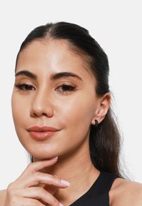 Boucles d'oreilles en métal noir en forme de créole ; texture lisse ; design circulaire ; portées sur l'oreille ; modèle avec des cheveux raides et une expression neutre.