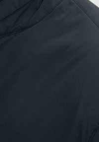 Tessuto scuro e liscio che mostra un primo piano della texture di una giacca. Presenta un design minimale senza motivi visibili o dettagli hardware.