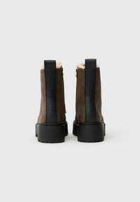 Botas de tobillo de cuero marrón con un acabado texturizado, suela de goma negra y forro de piel sintética. Cuentan con un cierre de cremallera y detalles con el logo.